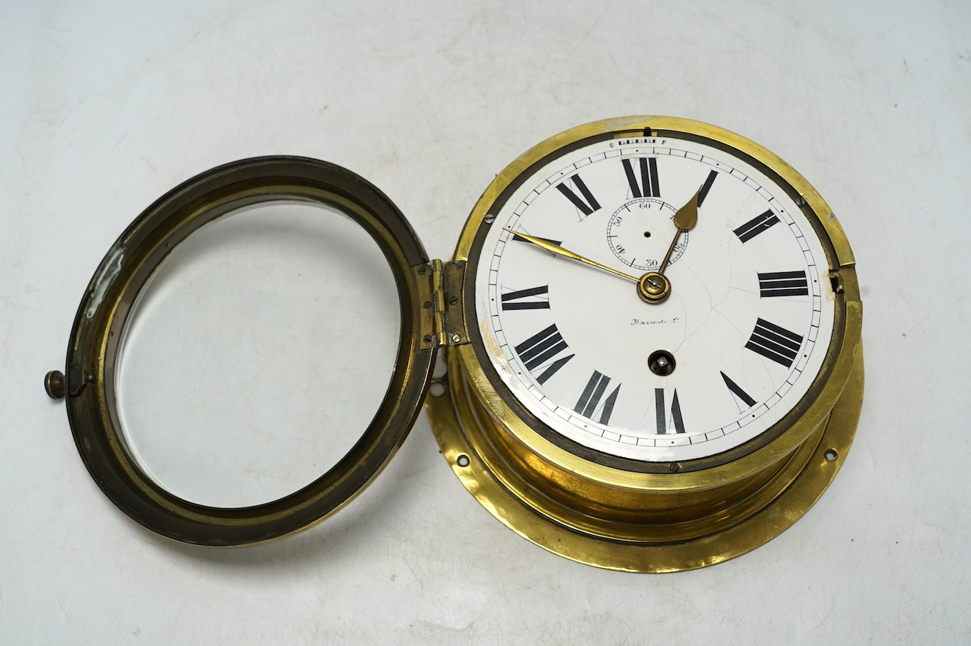 An early 20th century brass bulkhead timepiece retailed by Harrods, dial 13.5cm. Condition - poor to fair, seconds hand missing and some cracks to enamel dial